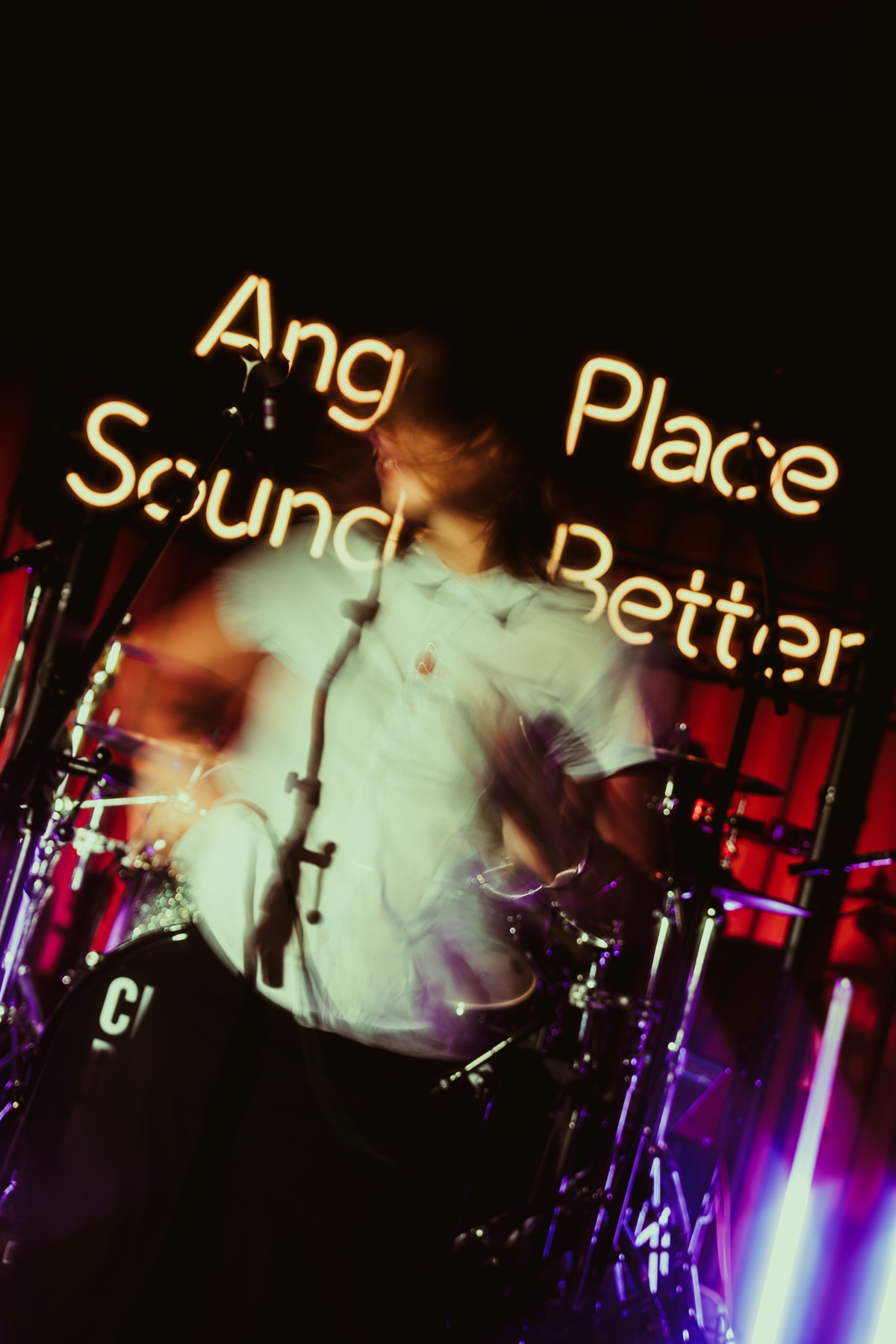 Performer under an 'Any Place Sounds Better' neon sign